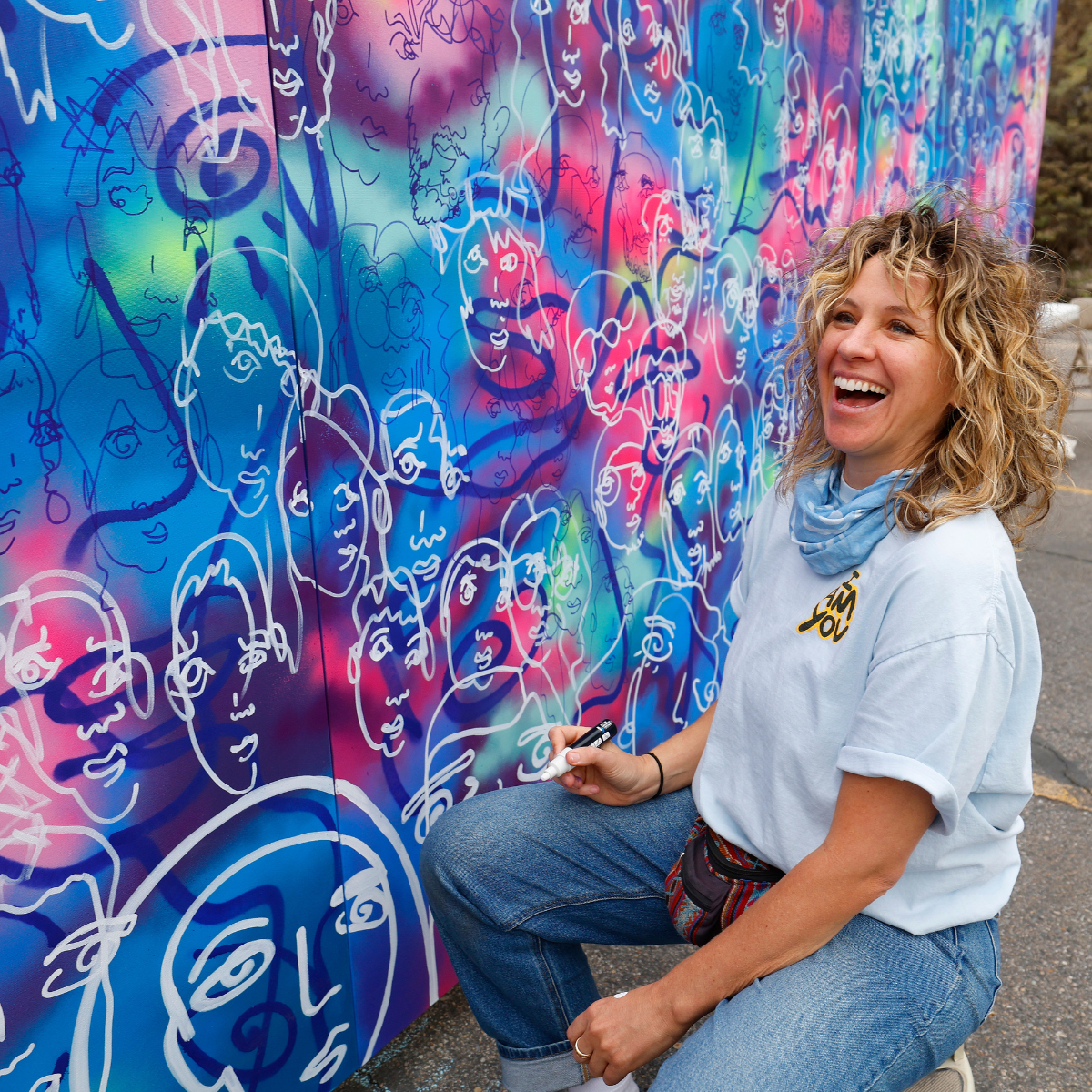 Woman laughing as she is activively painting on a mural